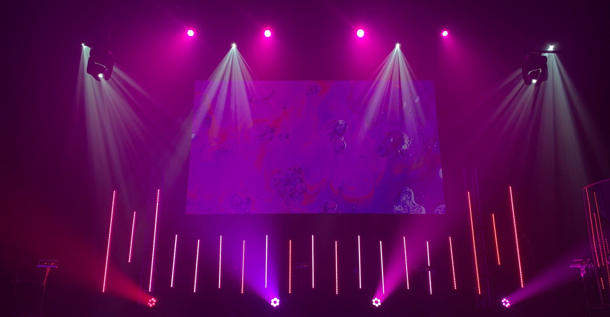 Stage with purple lighting and a large screen displaying abstract designs.